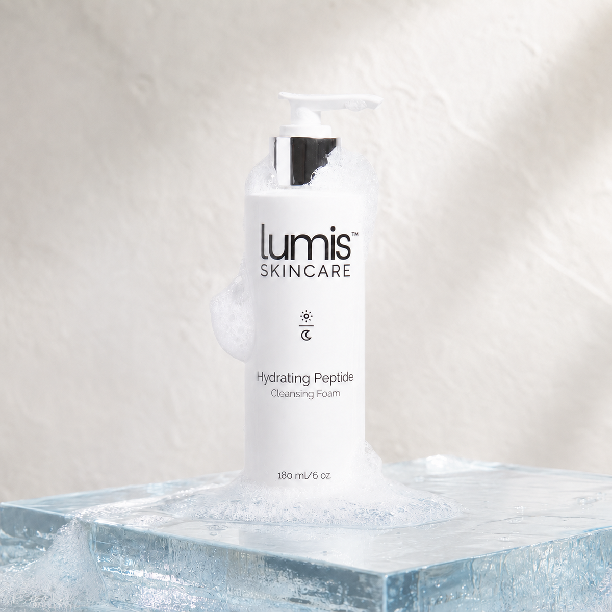 A white pump bottle of Lumis Skincare Hydrating Peptide Cleansing Foam sits on a clear ice block with foam dripping around it against a textured light beige background.