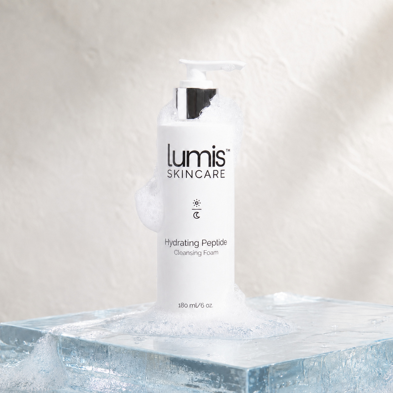 A white pump bottle of Lumis Skincare Hydrating Peptide Cleansing Foam sits on a clear ice block with foam dripping around it against a textured light beige background.